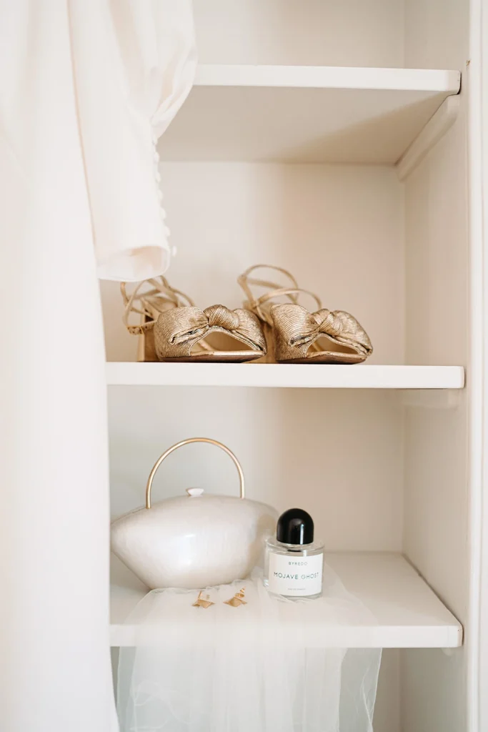 A close-up of the bride’s wedding accessories, including golden shoes, a pearl handbag, and perfume.