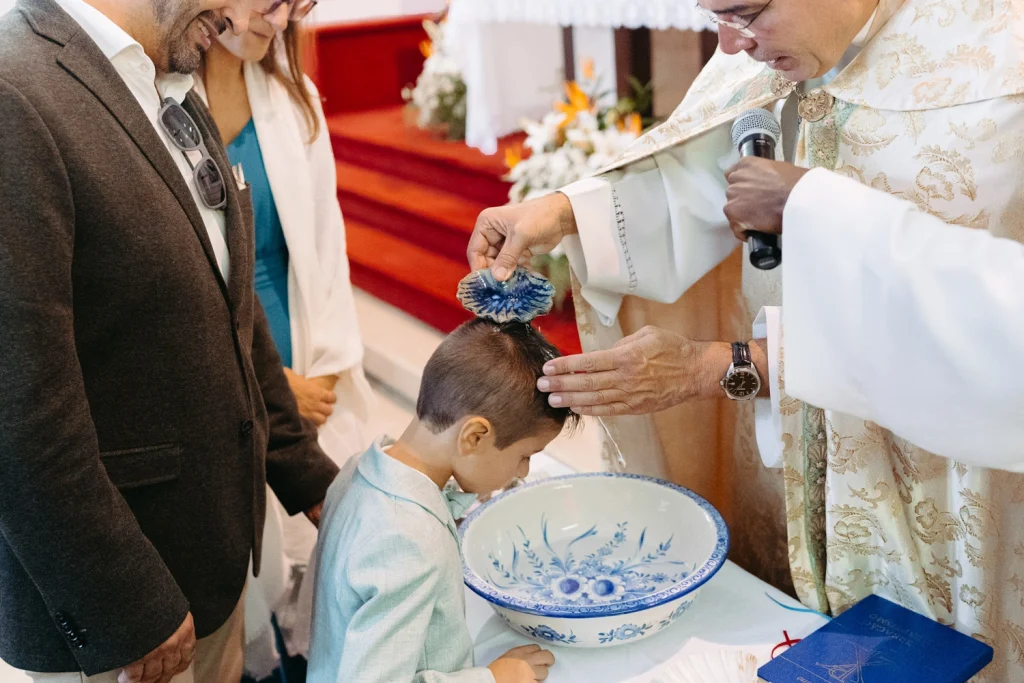 Priest pouring holy water on a young boy’s head during a baptism in a traditional Portuguese church.