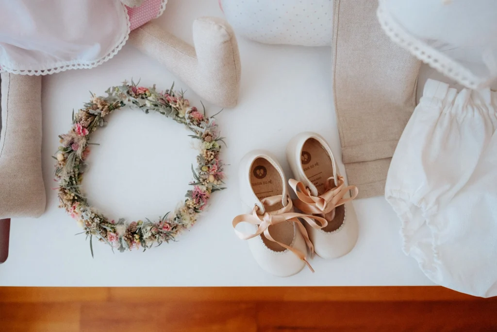 A delicate floral crown, baby shoes with satin ribbons, and baptism accessories arranged beautifully in Portugal.