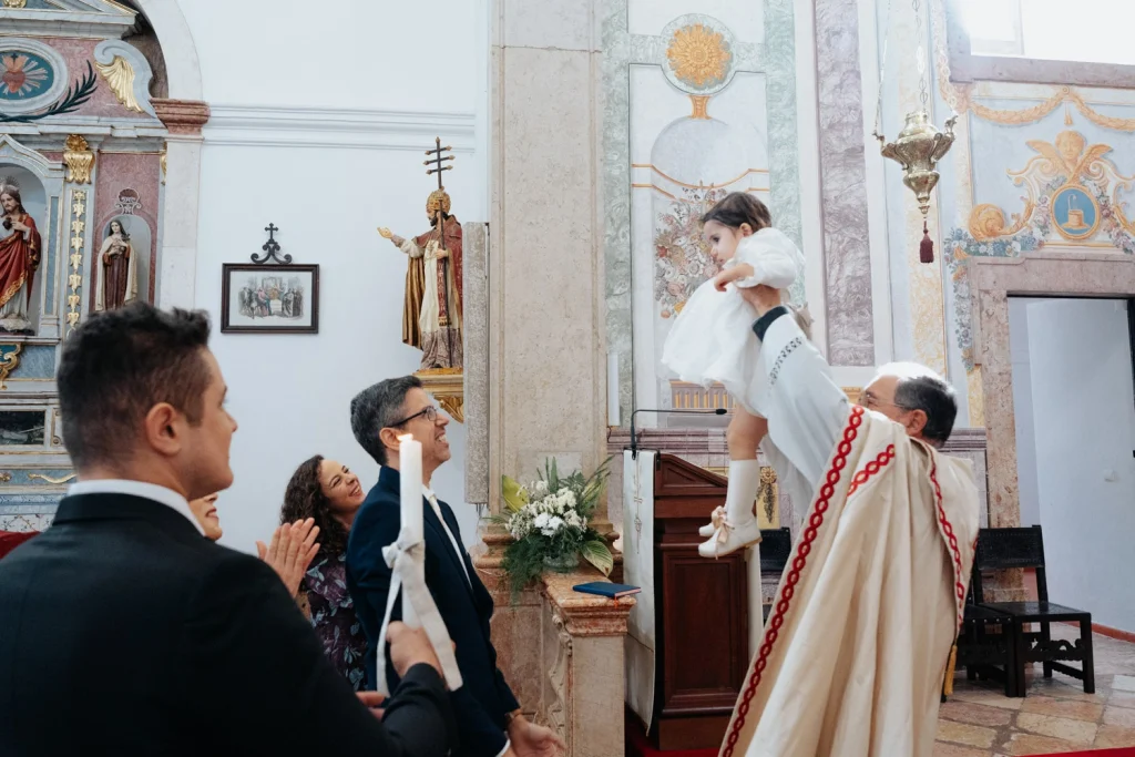 A priest lifting a baby in a touching baptism ceremony inside a historic church in Portugal.