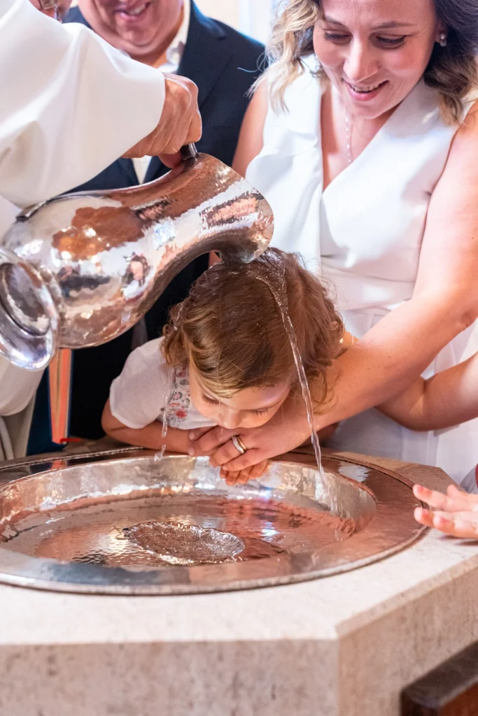 Holy water is poured over a child's head during a baptism ceremony, capturing a sacred moment of the ritual.