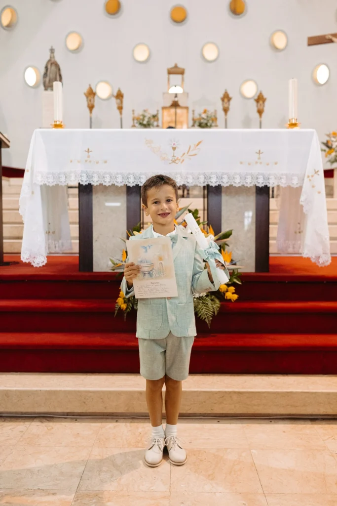 Young boy proudly holding his baptism certificate in front of the church altar