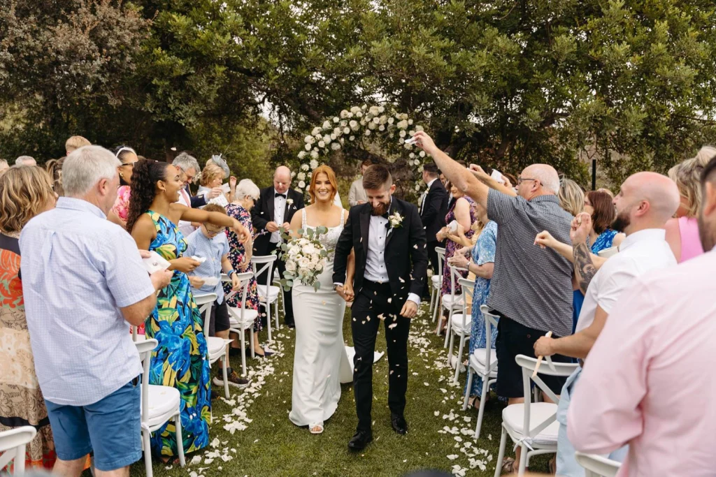 Newlyweds walk down the aisle as guests throw flower petals in celebration, capturing the joy of their special moment.