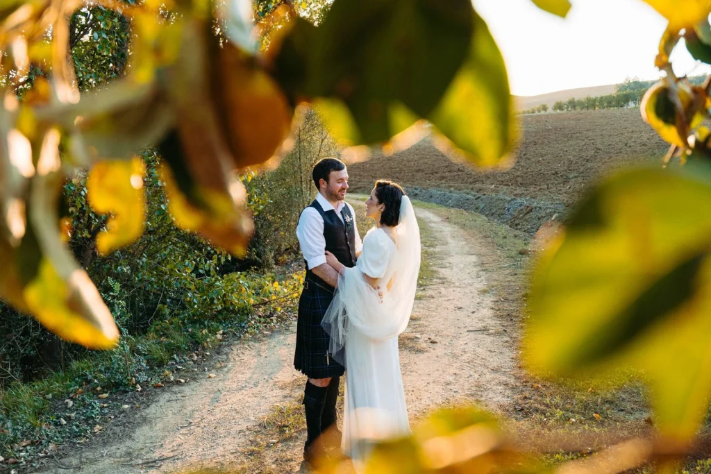 Bride and groom walking together down a scenic path at sunset, gazing into each other’s eyes.