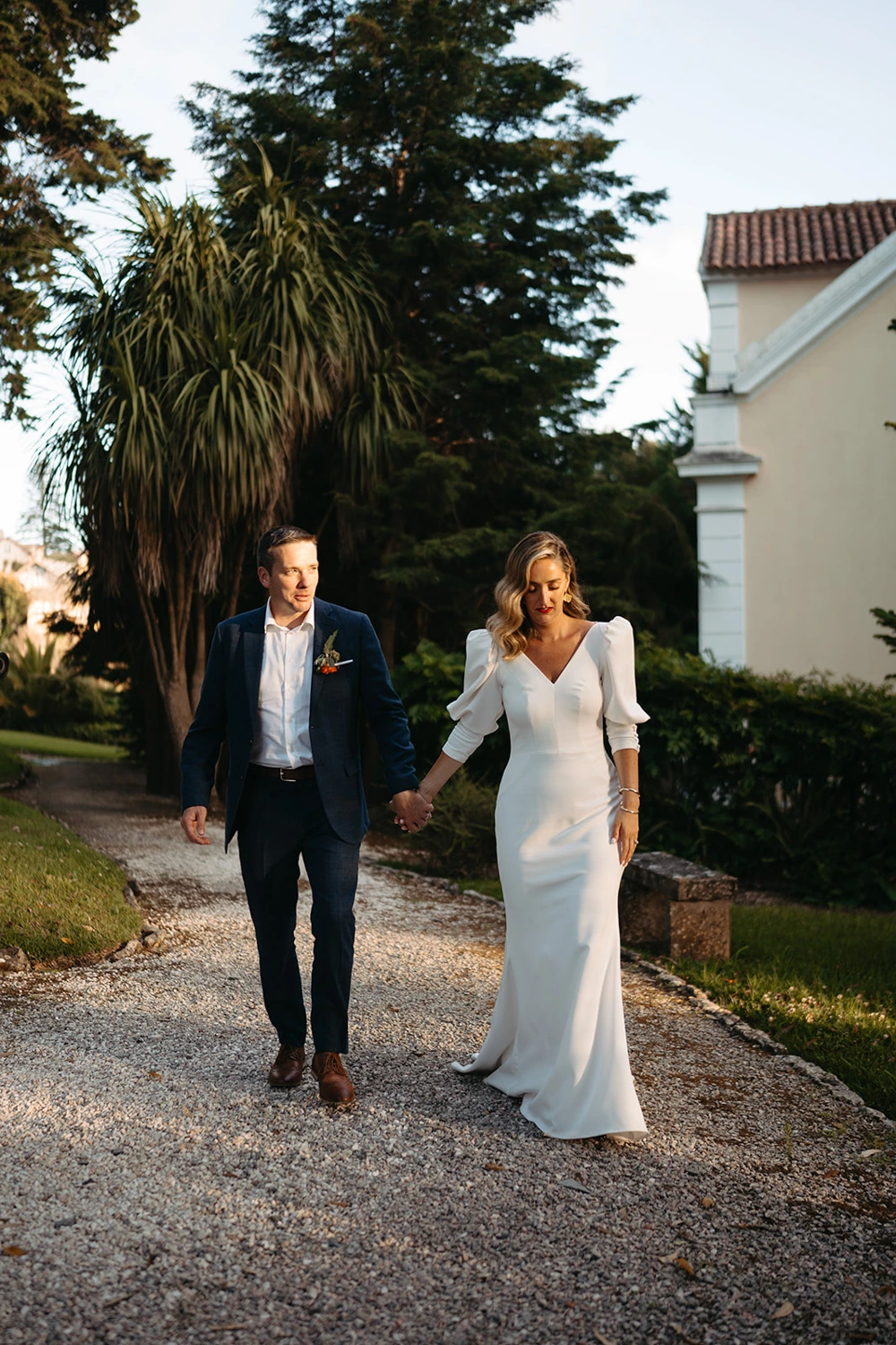 The bride and groom walking hand in hand along a scenic garden path, bathed in golden hour light.