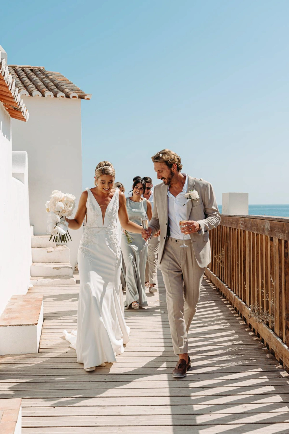 Bride in a white gown walking with her groom towards the wedding ceremony at a charming white chapel.