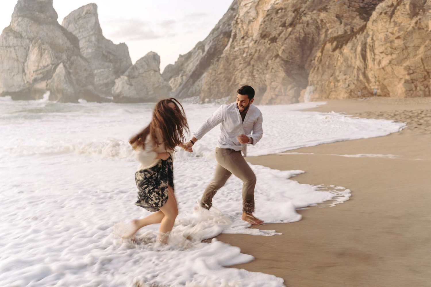 A joyful couple laughing together during a golden hour beach photoshoot in Portugal.