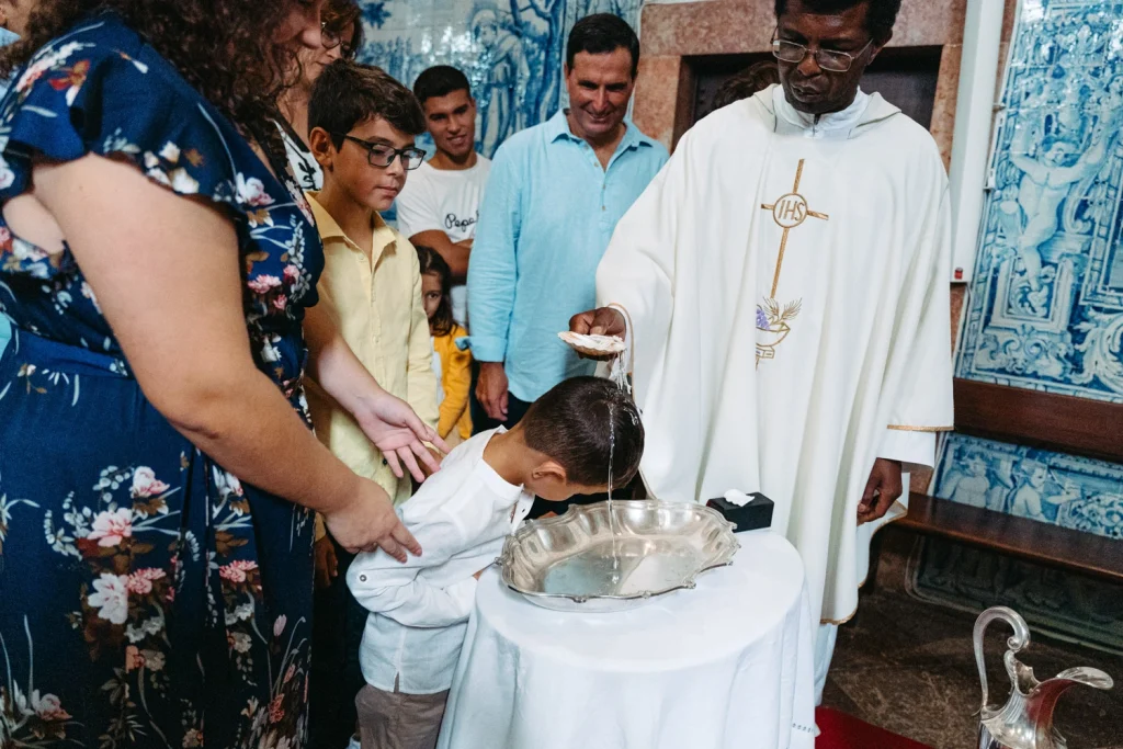 A young boy leans over a baptismal font as the priest pours holy water over his head.