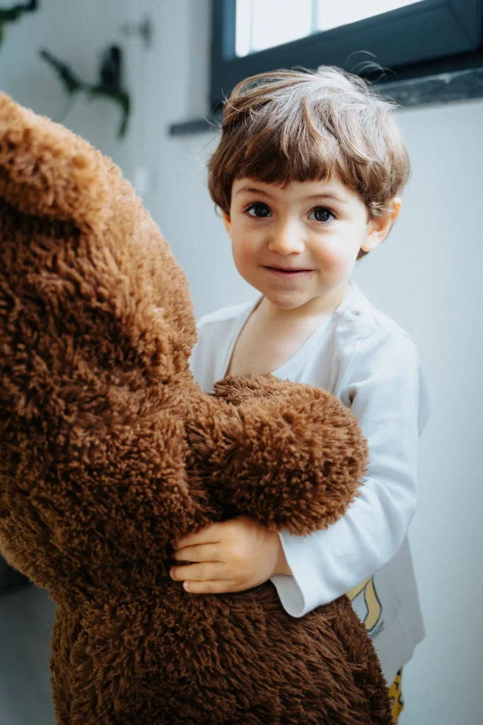 A young child hugging a large teddy bear, smiling with warm natural light in lisbon