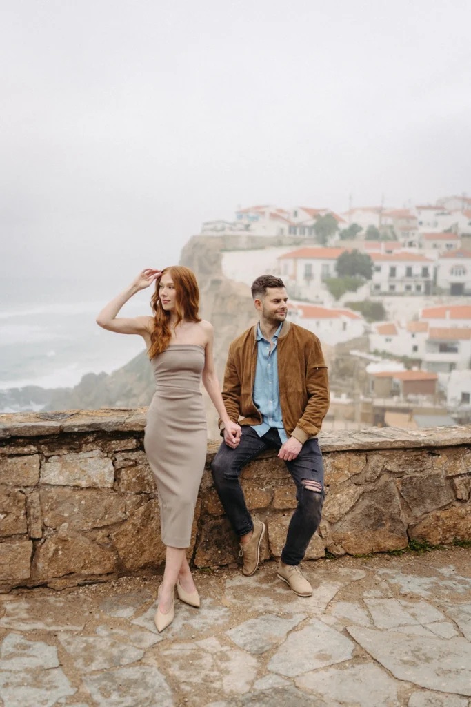 Couple embracing on a scenic coastal cliffside with waves crashing in the background during a maternity session in Portugal.