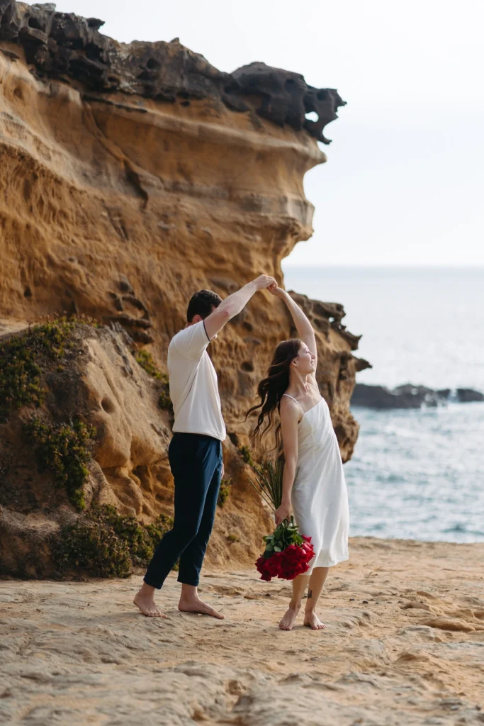 A couple twirling on a scenic cliffside, surrounded by ocean views and golden light.