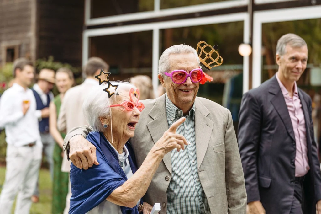 Elderly couple laughing with fun party glasses at a wedding celebration.