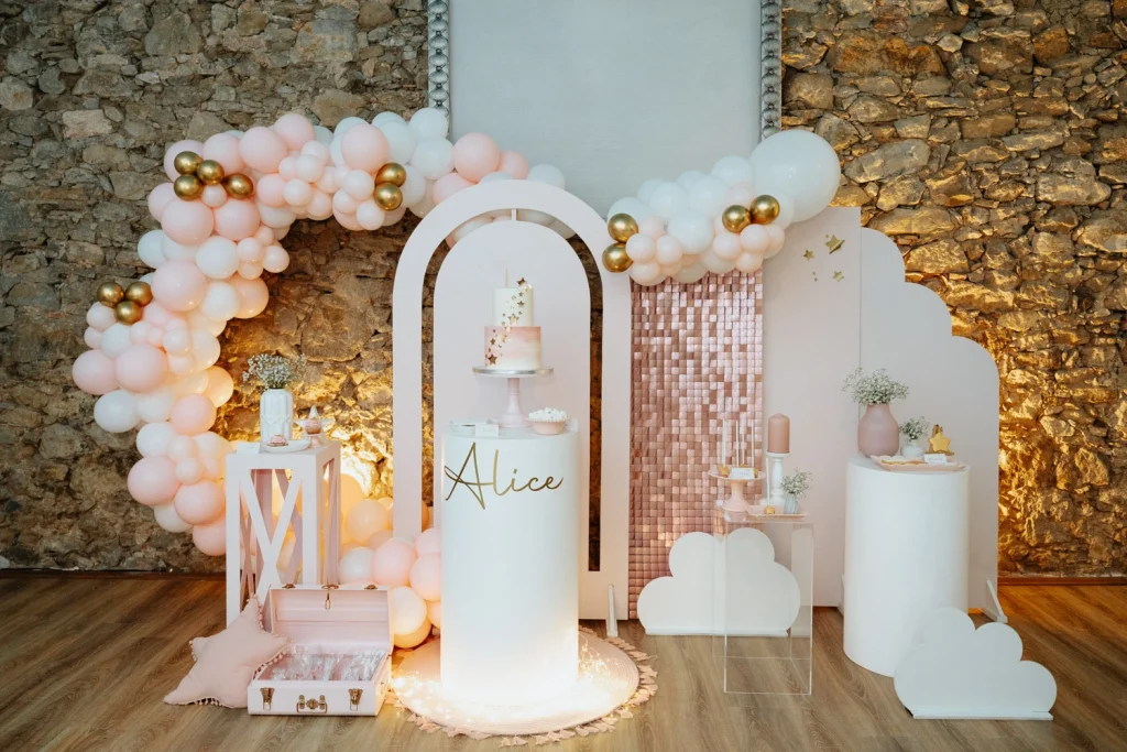 beautifully decorated baptism celebration setup with pink and gold balloons, a cake, and personalized details.