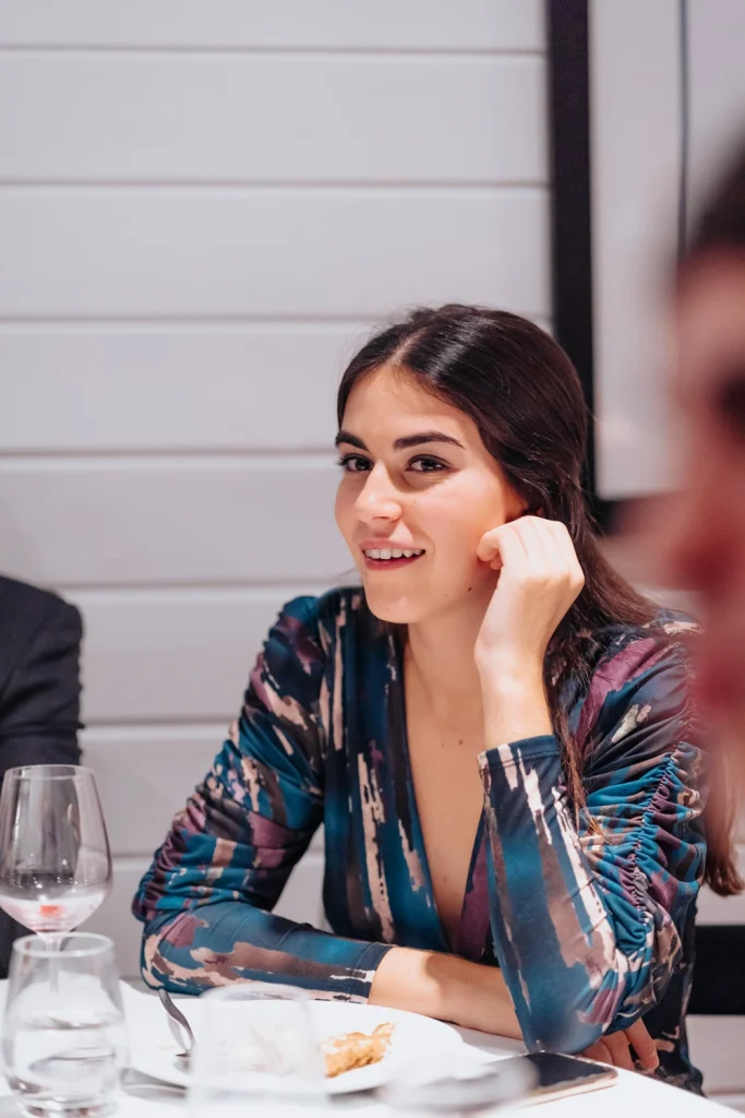 A stylish woman in an elegant blue dress smiles during an intimate dinner event, enjoying the warm ambiance in lisbon