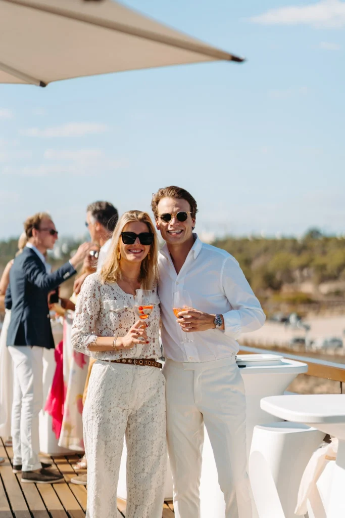 A stylish couple in white attire enjoying a cocktail toast at a luxurious rooftop event in Portugal.