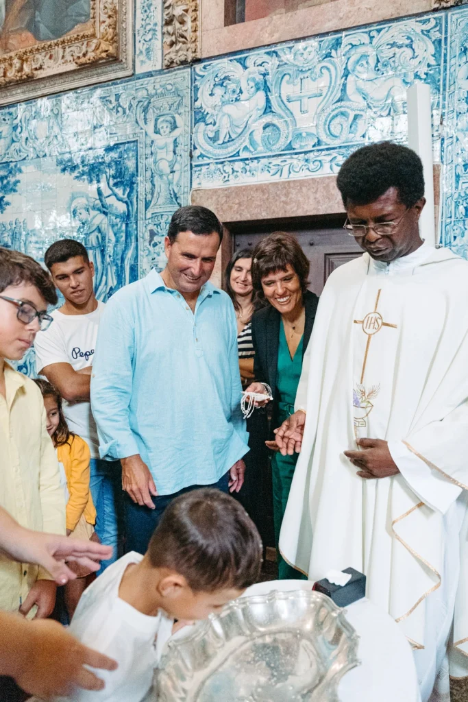 A smiling family surrounds their child as he receives the sacrament of baptism in a Portuguese church.