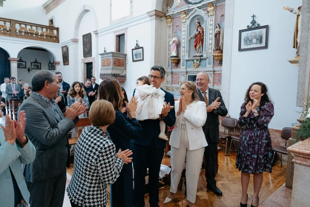 A joyful family claps and celebrates in a church after a baptism ceremony, surrounded by friends and loved ones.