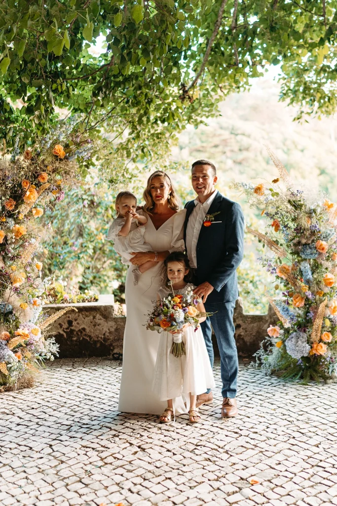 Bride, groom, and their children pose under a floral arch after the ceremony