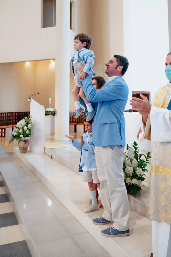 A proud father lifting his child during a baptism ceremony in a bright church.