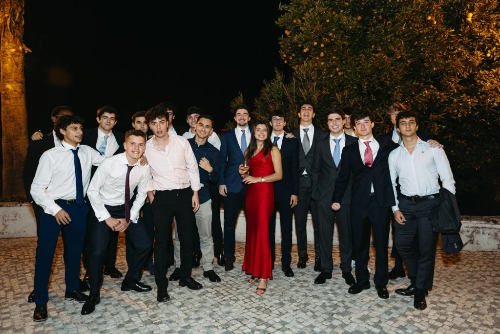 A group of young adults dressed in formal attire, smiling and celebrating under the night sky at an elegant event in Lisbon.