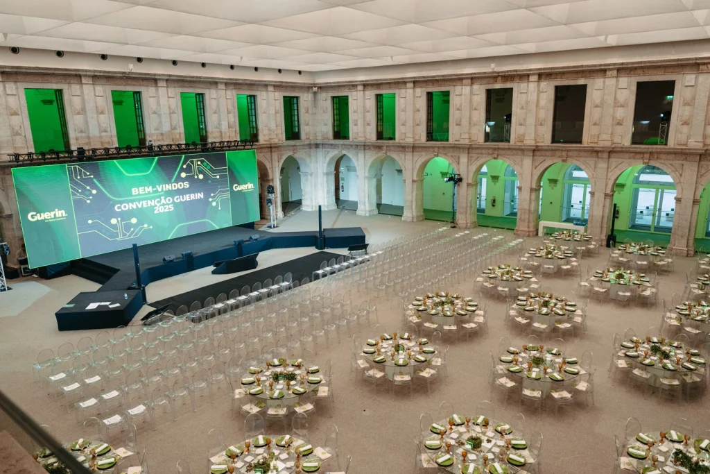 Overhead view of a beautifully set gala dinner venue with transparent chairs, sophisticated table decor, and a grand presentation stage ins Convento do Beato in Lisbon
