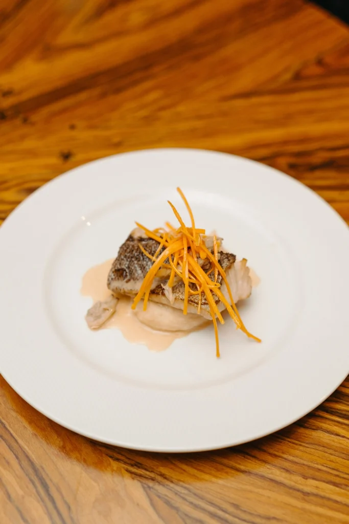 A beautifully plated gourmet fish dish with a creamy sauce and crispy carrot garnish, served at a high-end event in cascais