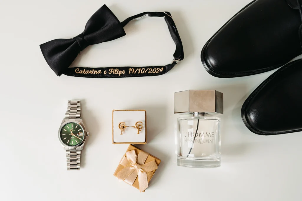 Groom’s wedding accessories, including a bow tie, cologne, cufflinks, and a watch, arranged elegantly for the big day.