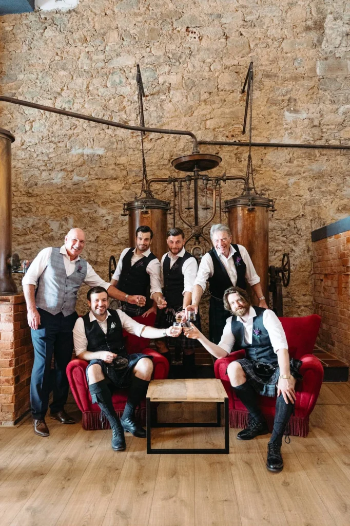 The groom and his groomsmen posing in a historic distillery, surrounded by vintage copper stills and exposed stone walls in quinta da bichinha