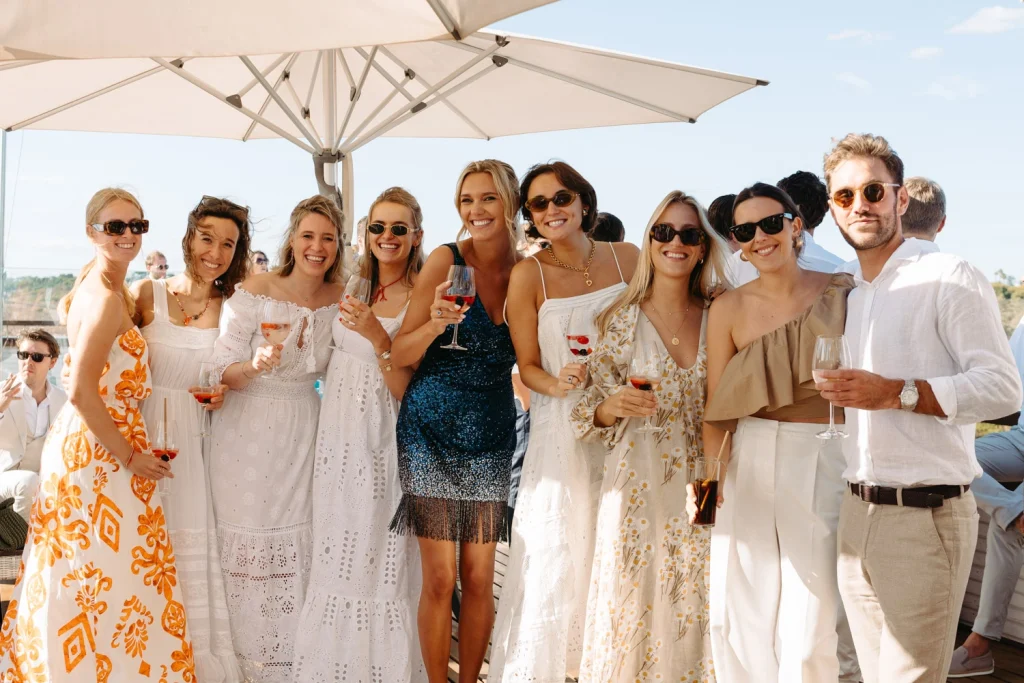 A joyful group of friends raising glasses in celebration at a beautiful outdoor event with ocean views.