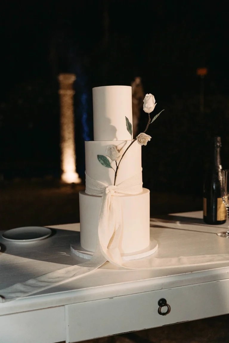 Minimalist three-tier wedding cake with elegant white floral details and a soft fabric bow.