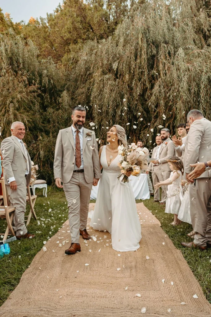 Just-married couple walks down the aisle, laughing and celebrating as guests throw flower petals during a beautiful outdoor wedding ceremony in Lisbon.