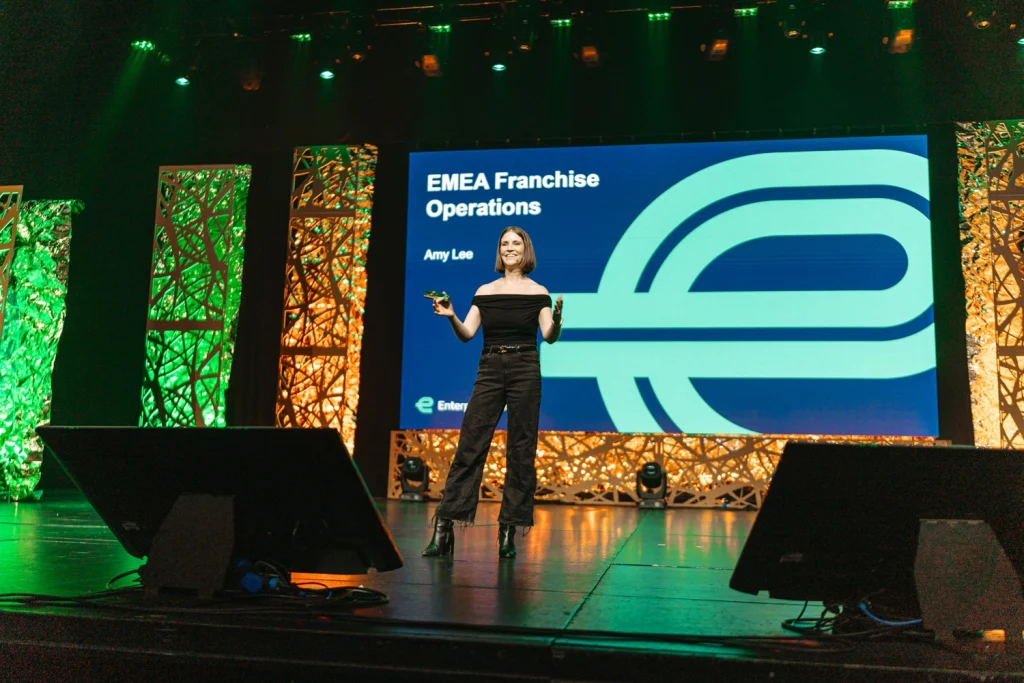 A confident keynote speaker addressing a business audience on a grand stage at a professional event in Lisbon in Convento do Beato