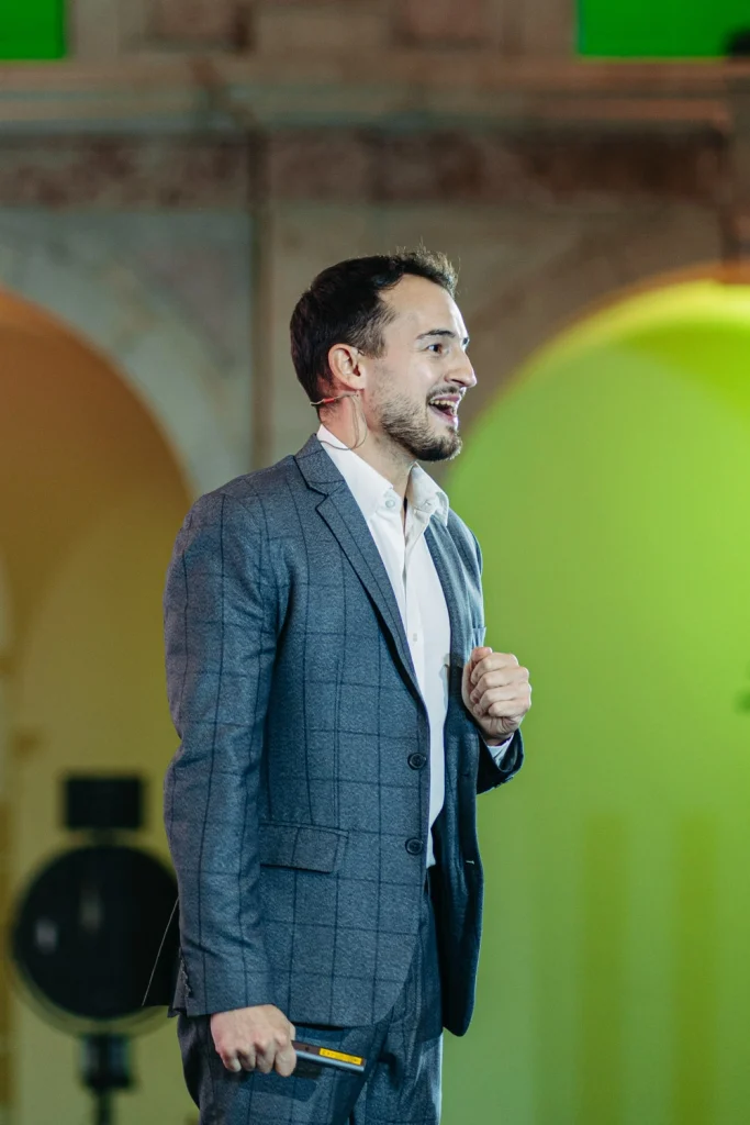 A confident keynote speaker in a tailored suit delivering a speech at a professional conference event.