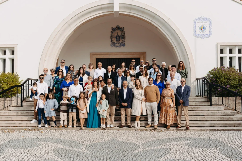 A large family gathered for a group photo outside a Portuguese church after a baptism ceremony.