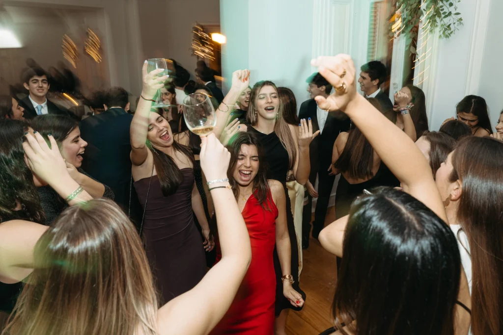 A group of young women dancing with excitement at a birthday party, raising glasses and enjoying the moment.
