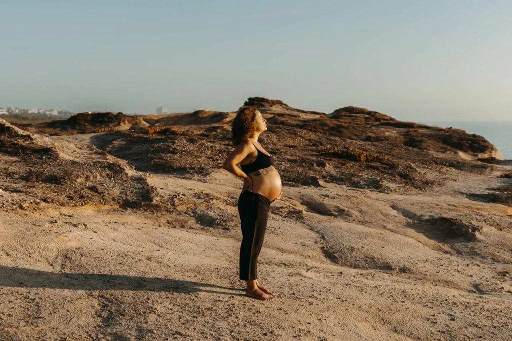 Pregnant woman standing barefoot on a scenic Portugal coastline as seagulls soar in the background during golden hour