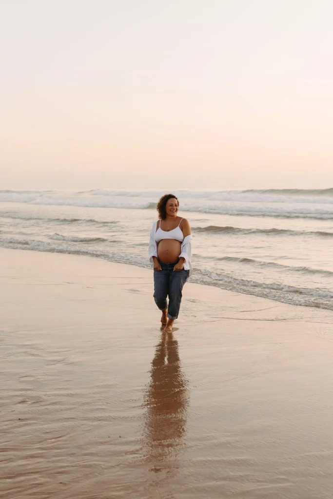 Serene maternity portrait of a woman embracing her pregnancy, bathed in golden hour light with the ocean behind her