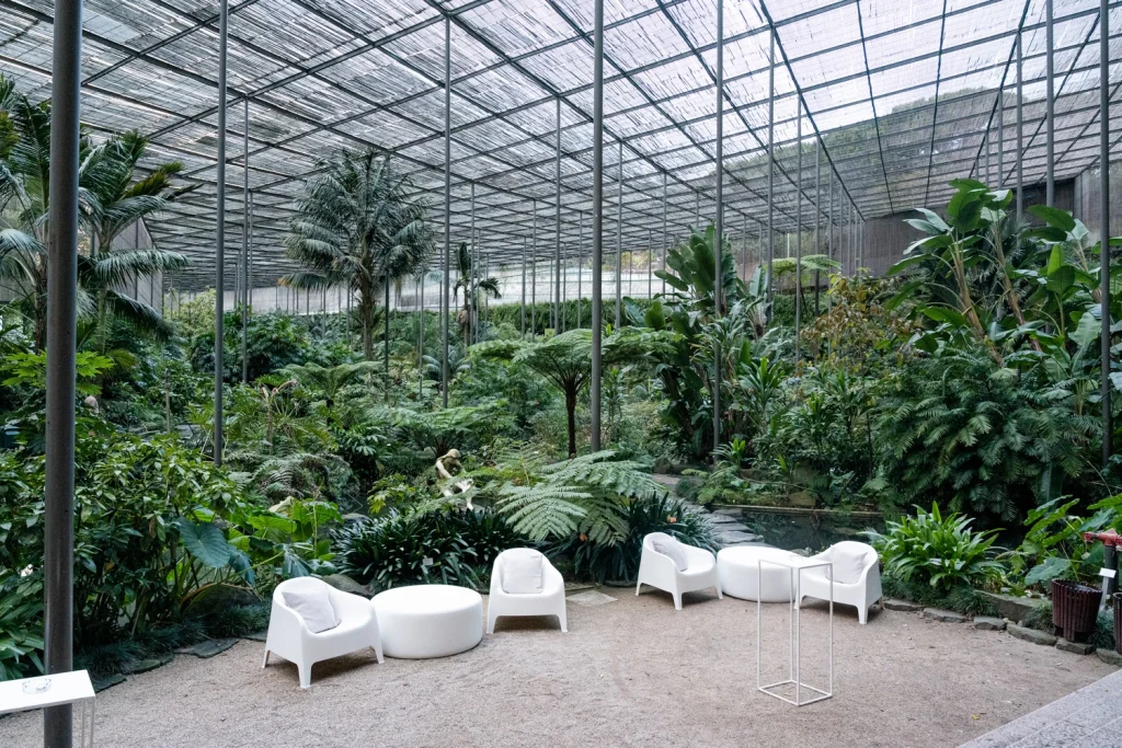 A lush greenhouse venue set up for an elegant event, featuring white lounge seating and tropical plants in estufa fria in lisbon
