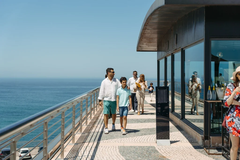A stylish family walks along an oceanfront terrace, enjoying the scenic coastal view on a sunny day in ericeira