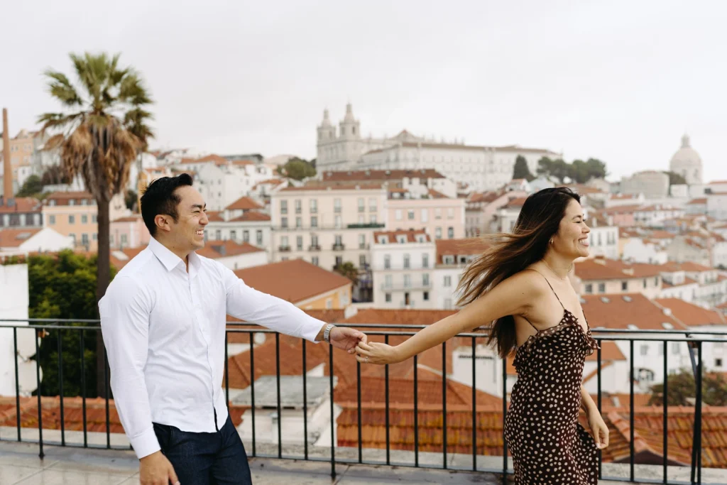 A couple leans against a historic Lisbon balcony, the warm sunset reflecting their love and laughter
