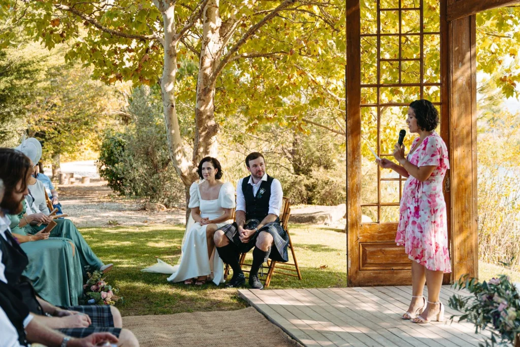 A breathtaking outdoor wedding ceremony by the lake, framed by golden trees and rustic wooden doors.