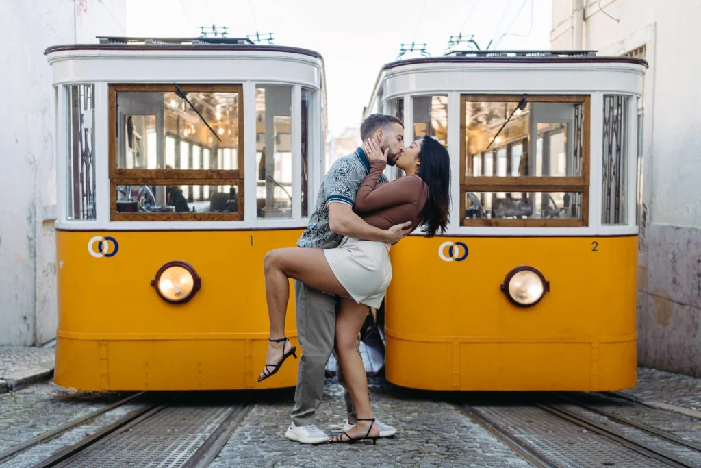 A couple passionately kisses between two yellow trams in Lisbon, a dreamy and cinematic engagement photo