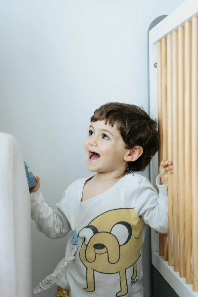 A joyful toddler laughing in his bedroom, holding a toy near his crib