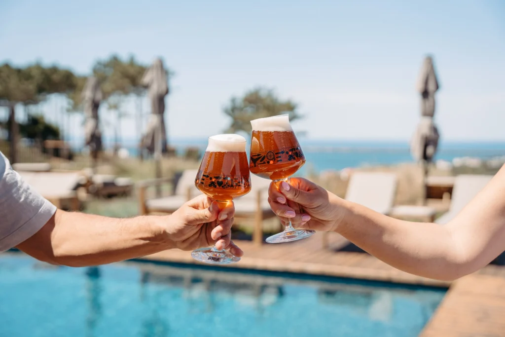 A couple clinking glasses of craft beer by the poolside, celebrating a relaxed getaway.