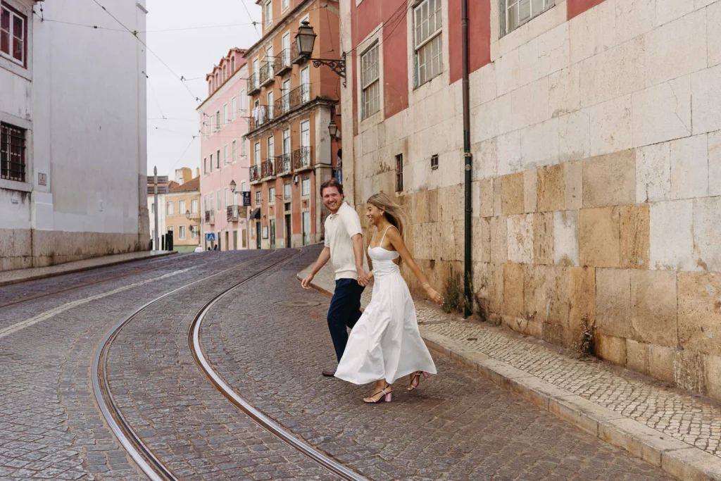 A joyful couple shares a romantic moment in Lisbon’s Alfama neighborhood, with the historic cityscape behind them.