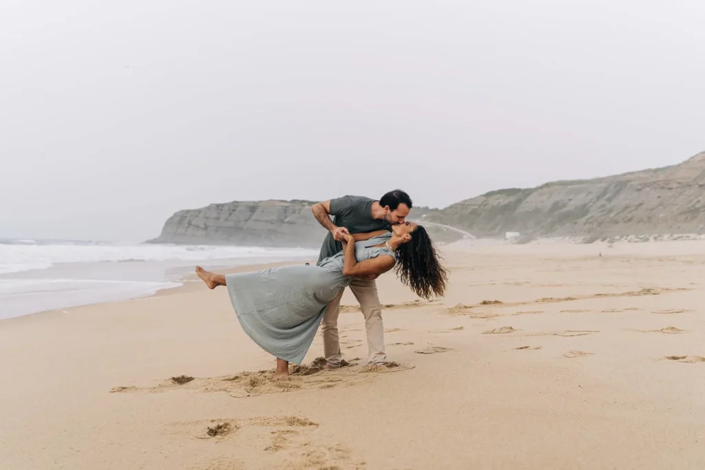Couple sharing a passionate dance on the sandy shores of Portugal, waves crashing behind them