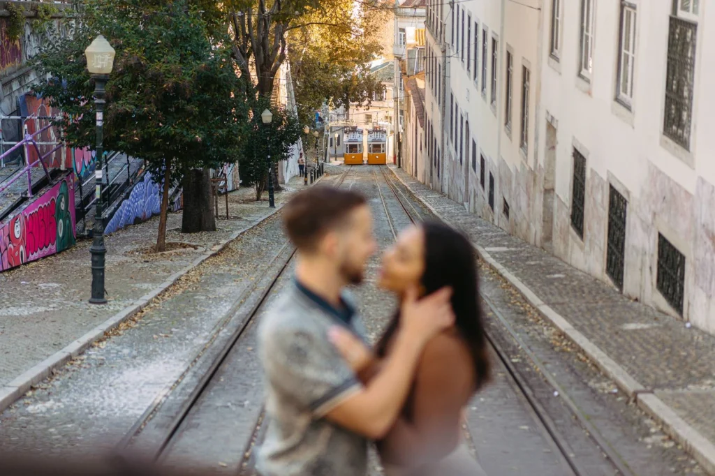 A romantic couple shares an intimate moment with the iconic yellow trams of Lisbon in the background.