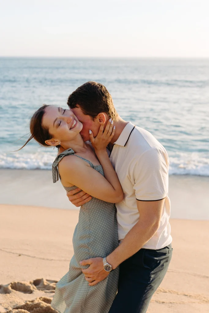 A couple sharing a heartfelt embrace on the beach, bathed in warm sunset light.