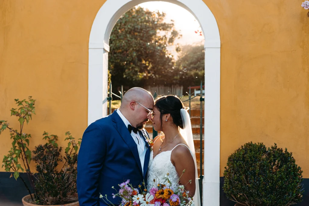 Bride and groom embracing under a canopy of leaves, basking in the glow of their wedding day. in quinta de santana