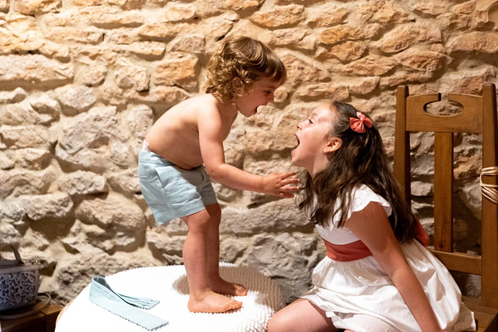 A young boy and his older sister share a joyful moment, laughing together during a baptism celebration.